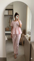Woman wearing baby pink bow print peplum night suit with relaxed fit pants, soft comfortable lounge wear set.