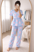 Woman wearing Blush Whispers sky blue peplum night suit with pink star prints and full-length pants, taking a mirror selfie in a cozy bedroom.