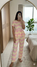 Woman wearing pastel pink and cream chevron print peplum night suit with relaxed fit pants, soft comfortable homewear set.